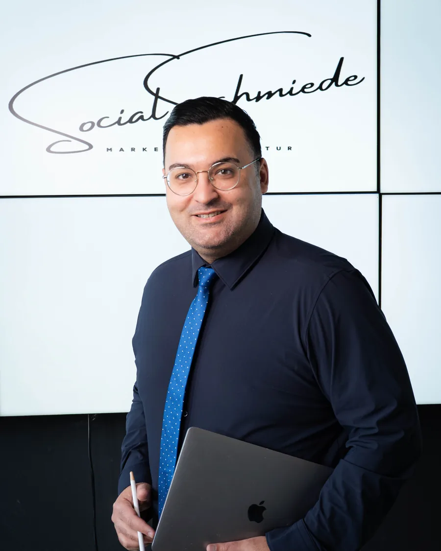 Ercan Caliskan, Gründer von SocialSchmiede, vor dem Firmenlogo in Menden